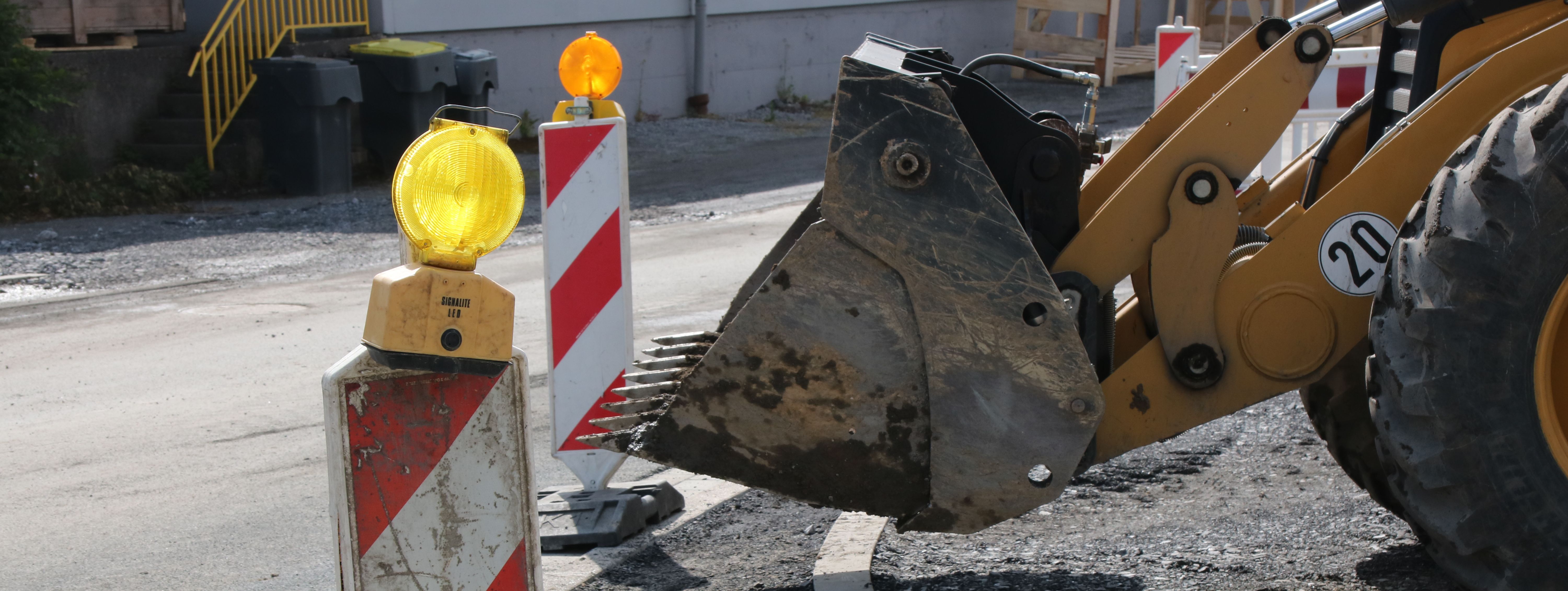 Im Vordergrund steht eine rot-weiße Bake mit gelber Warnleuchte darauf, im Hintergrund sieht man die Schaufel eines Radladers.