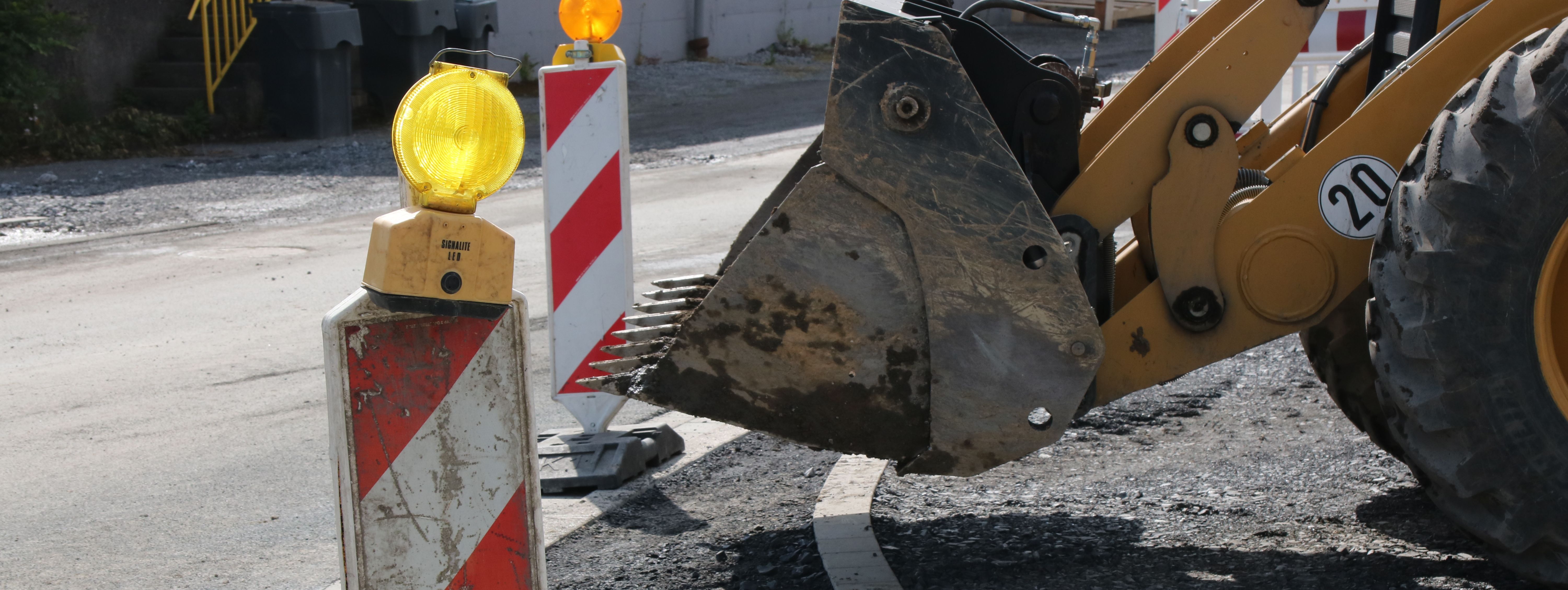 Im Vordergrund steht eine rot-weiße Bake mit gelber Warnleuchte darauf, im Hintergrund sieht man die Schaufel eines Radladers.