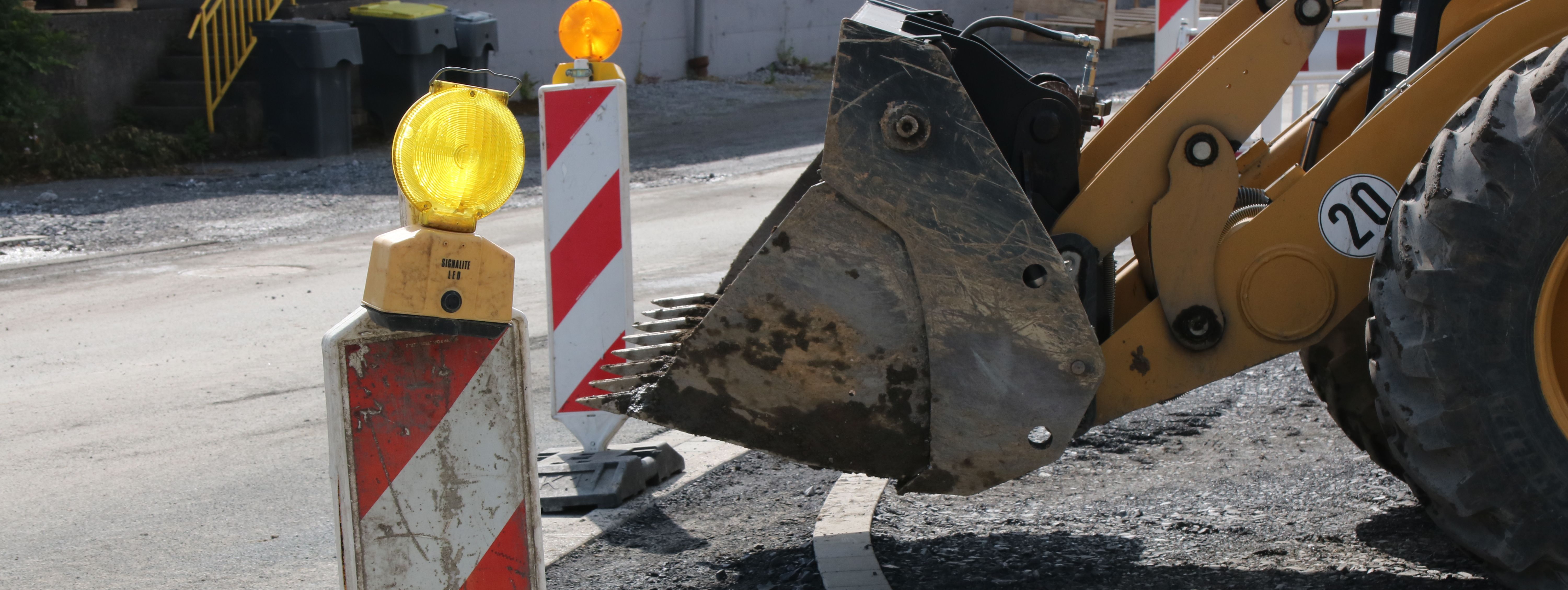 Im Vordergrund steht eine rot-weiße Bake mit gelber Warnleuchte darauf, im Hintergrund sieht man die Schaufel eines Radladers.