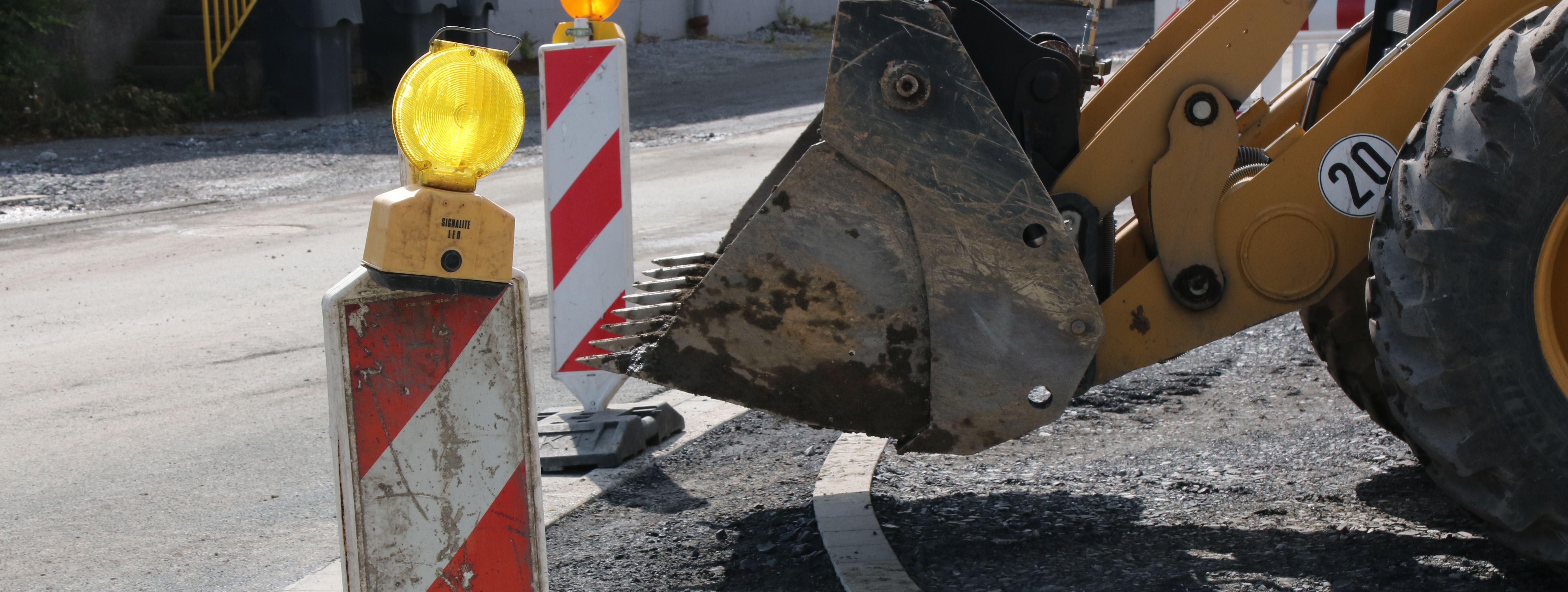 Im Vordergrund steht eine rot-weiße Bake mit gelber Warnleuchte darauf, im Hintergrund sieht man die Schaufel eines Radladers.