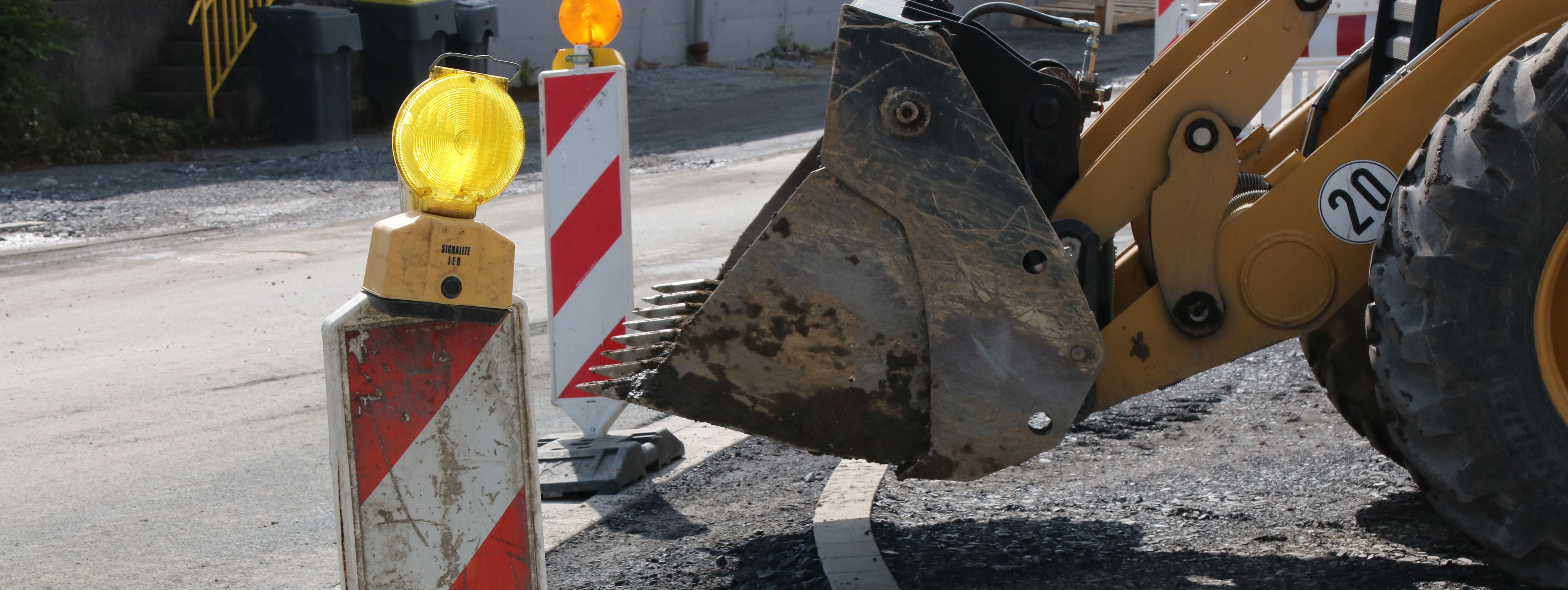 Im Vordergrund steht eine rot-weiße Bake mit gelber Warnleuchte darauf, im Hintergrund sieht man die Schaufel eines Radladers.