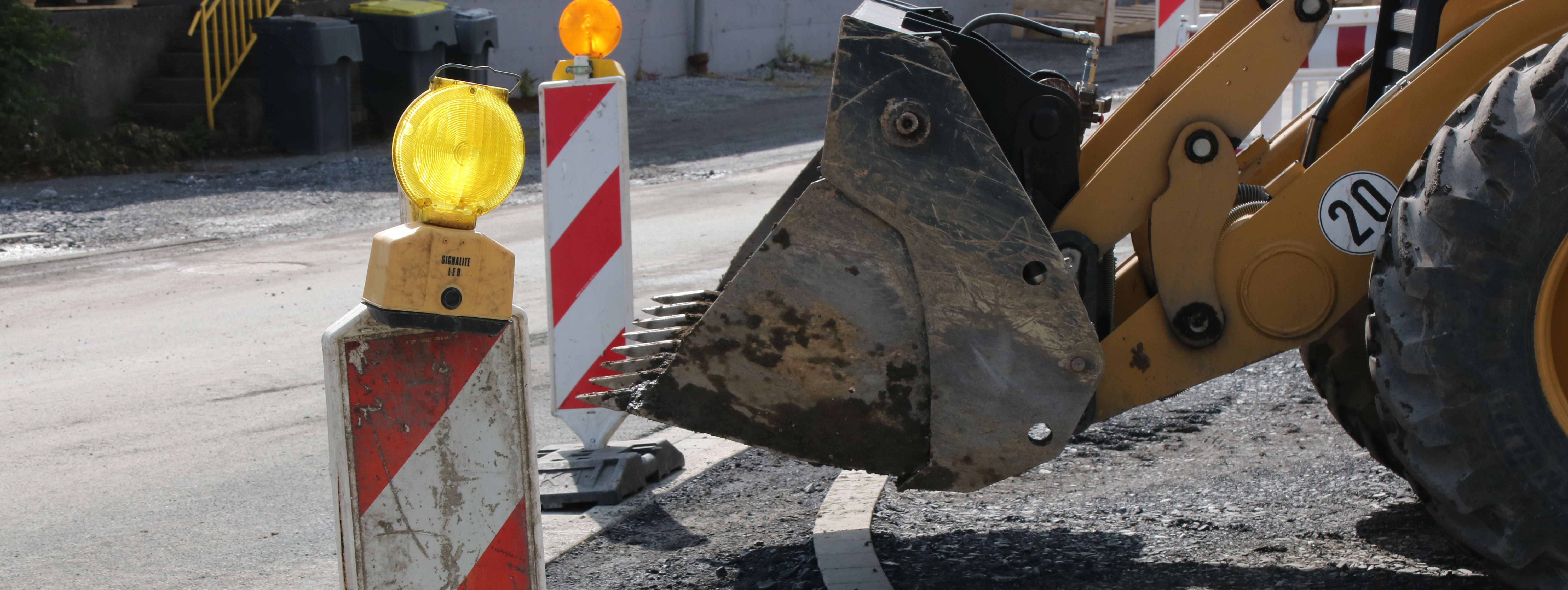 Im Vordergrund steht eine rot-weiße Bake mit gelber Warnleuchte darauf, im Hintergrund sieht man die Schaufel eines Radladers.