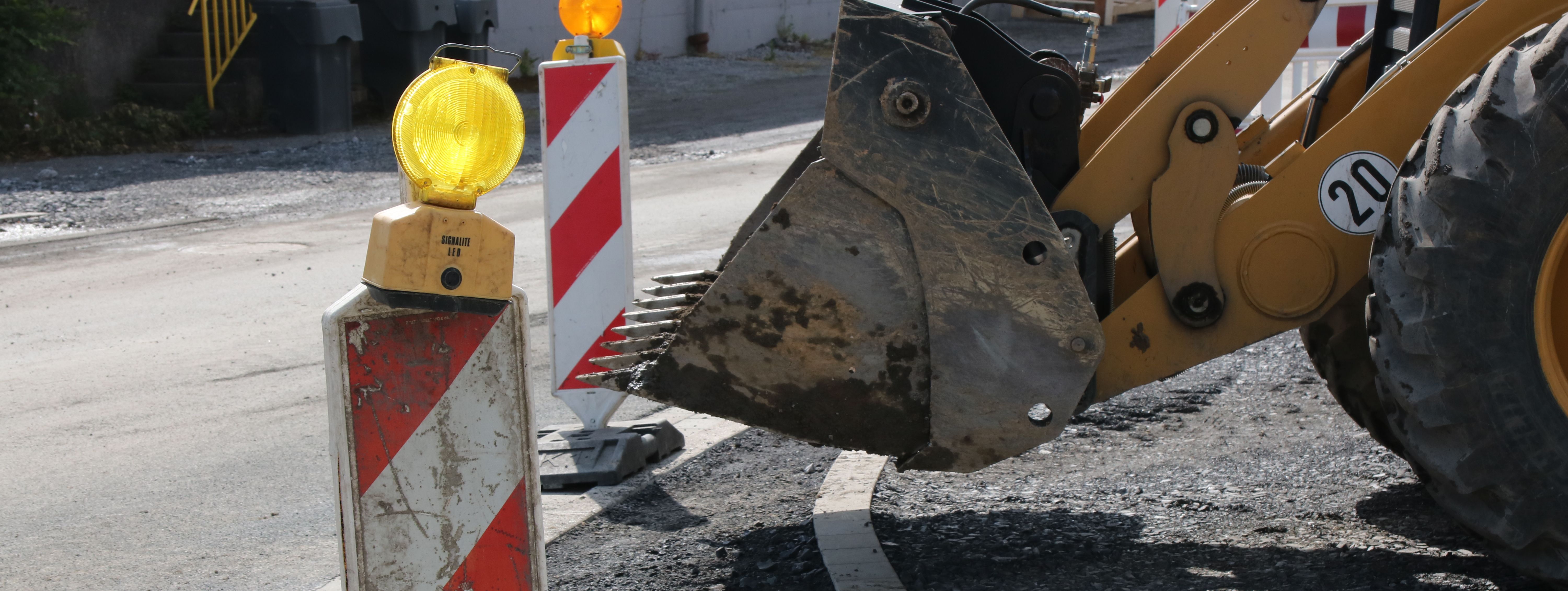 Im Vordergrund steht eine rot-weiße Bake mit gelber Warnleuchte darauf, im Hintergrund sieht man die Schaufel eines Radladers.