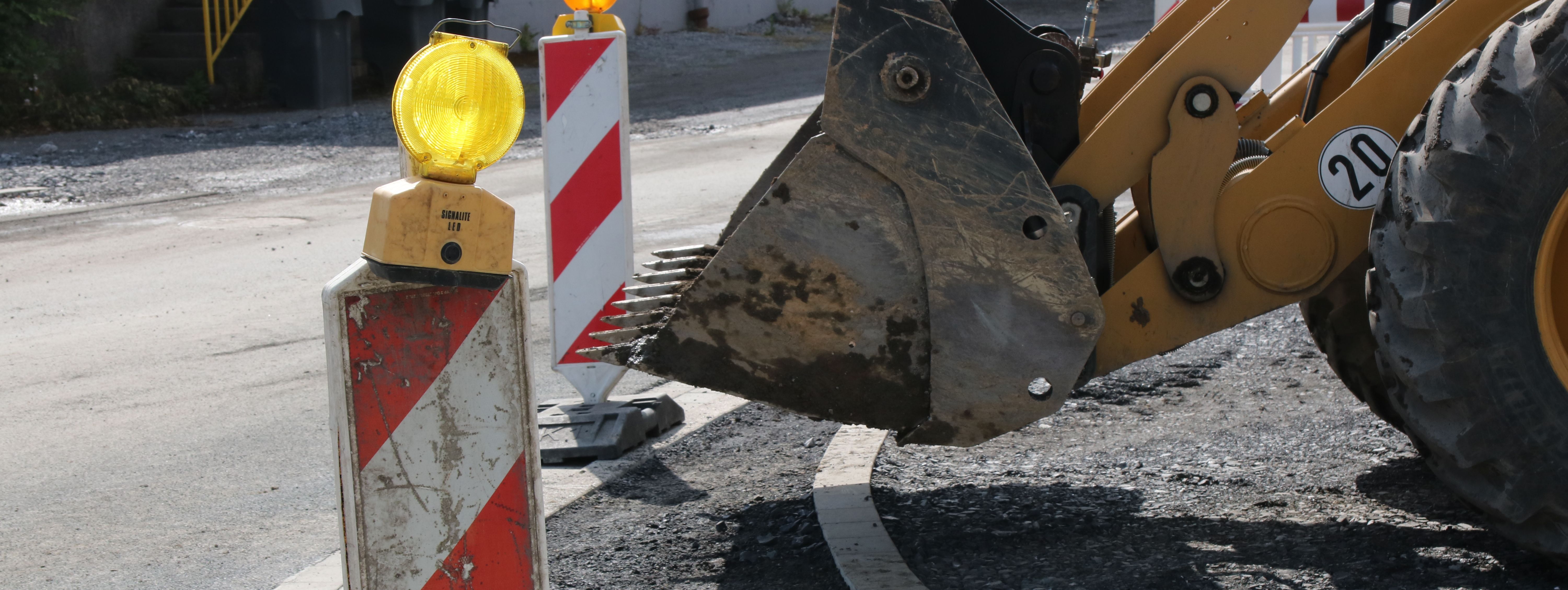 Im Vordergrund steht eine rot-weiße Bake mit gelber Warnleuchte darauf, im Hintergrund sieht man die Schaufel eines Radladers.