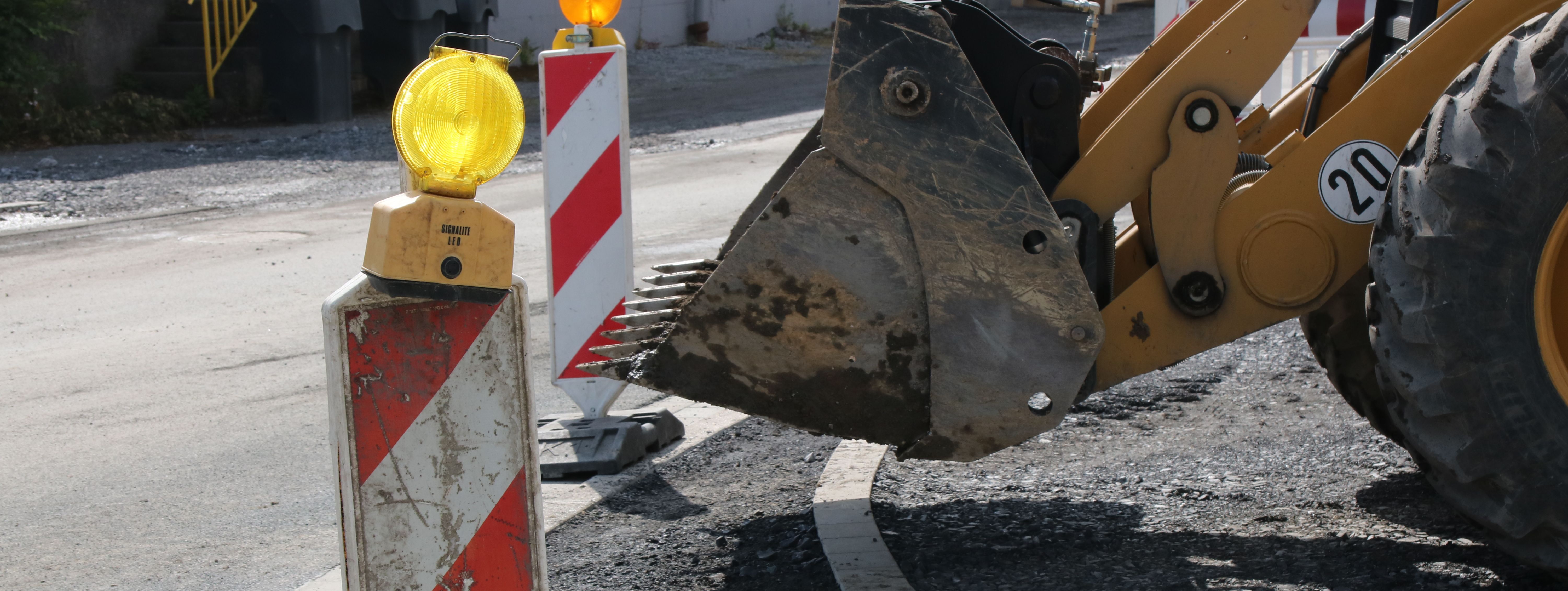 Im Vordergrund steht eine rot-weiße Bake mit gelber Warnleuchte darauf, im Hintergrund sieht man die Schaufel eines Radladers.