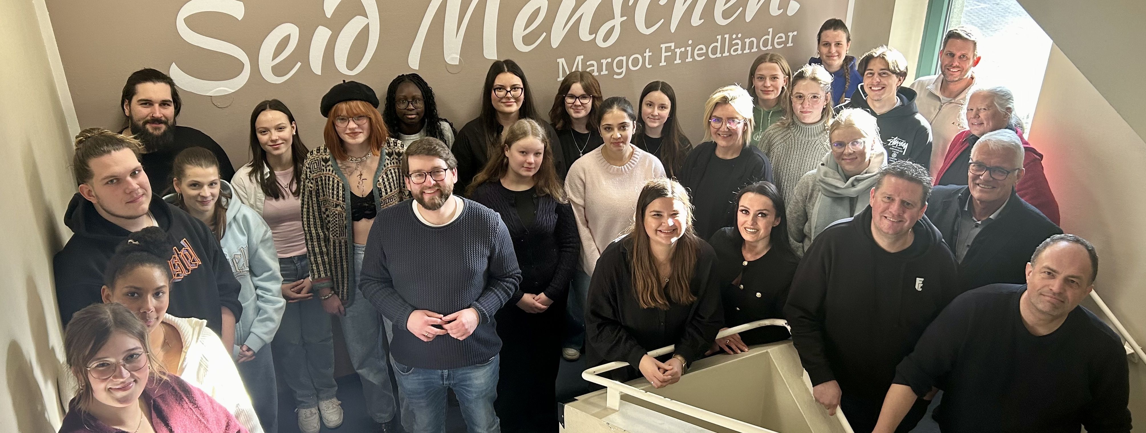 Mendener Schülerinnen und Schüler des Netzwerkes "augen auf!" vor der Inschrift des Margot Friedländer-Zitates "Seid Menschen" im Treppenhaus des Neuen Rathauses.