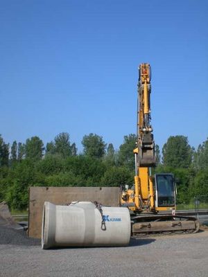 Bagger, Kanalrohre mit rd. einem Meter Durchmesser und Verbautafeln aus Stahl zur Absicherung der Baugrube stehen zum Einsatz auf einer Baustelle bereit.