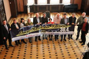 12 Personen stehen im Alten Ratssaal nebeneinander und halten ein Banner hoch