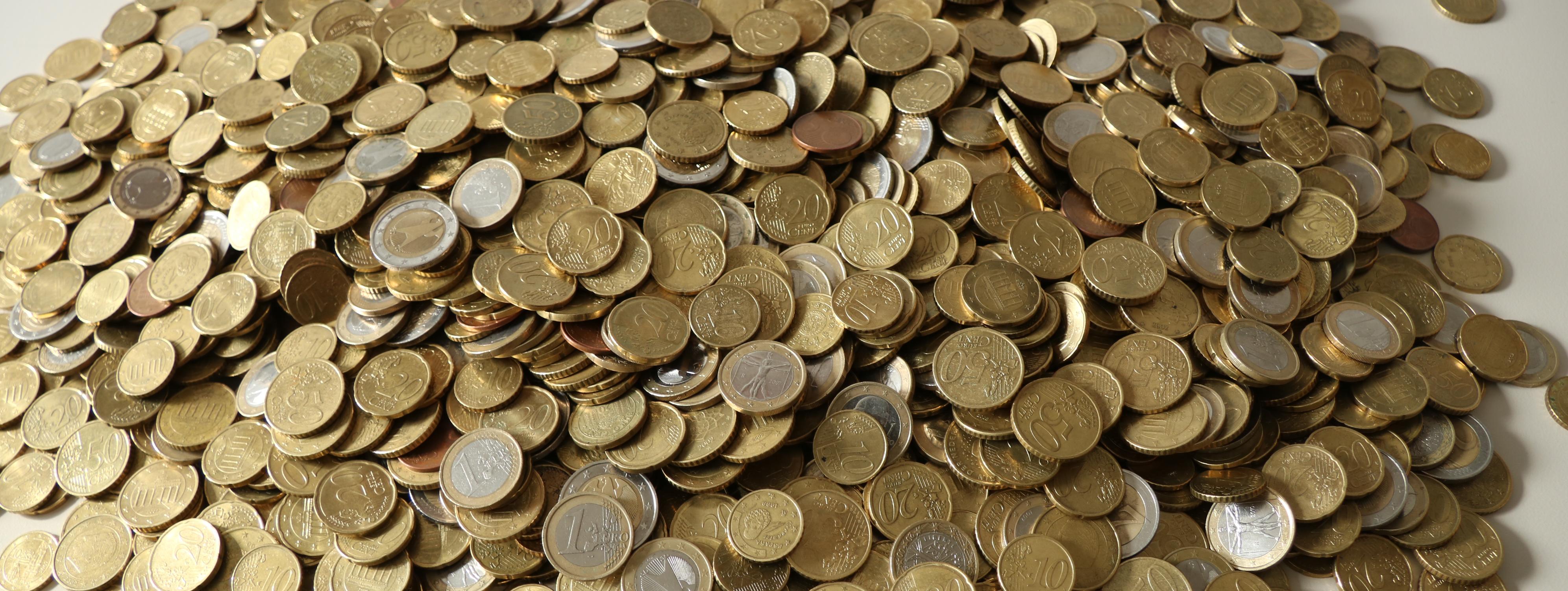 Auf einem weißen Tisch liegen zahllose Euro-Münzen auf einem großen Haufen.