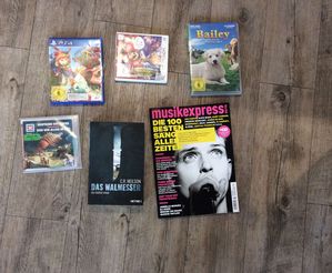 Jeweils ein(e) CD, PS 4-Spiel, Nintendo 3 DS-Spiel, DVD, Zeitschrift und Buch auf grauem Fußboden