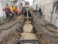 Im Zuge der Erneuerung der Innenstadt 2017 wurden in der Hoch- und Kirchstraße auch die Kanalrohre erneuert. Wegen der beengten Platzverhältnisse in der Baugrube und des schwierigen Baugrundes erfolgte die Umhüllung der neuen Rohre sowie die Verfüllung der Baugrube mit Flüssigboden. Dieser wird - ähnlich wie Beton - in die Baugrube eingefüllt und schließt alle vorhandenen offenen Bereiche, insbesondere auch zwischen den Versorgungsleitungen. Im Gegensatz zu Beton ist der Flüssigboden nach der Aushärtung aber "spatenfest", d.h. er kann mit einfachen Mitteln wieder gelöst und ausgebaut werden. Auf dem Foto ist die Verfüllung der Kanalbaugrube in der Hochstraße zu sehen, der Boden fließt von einem Lkw mit Mischtrommel direkt in die Baugrube (Foto: Stadtentwässerung).