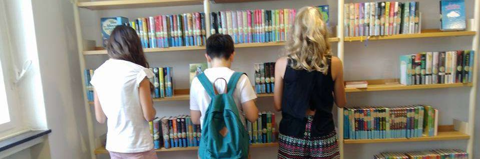 drei Jugendliche stehen vor einem Bücherregal in der Stadtbücherei und suchen sich Lesestoff für die Sommerferien aus