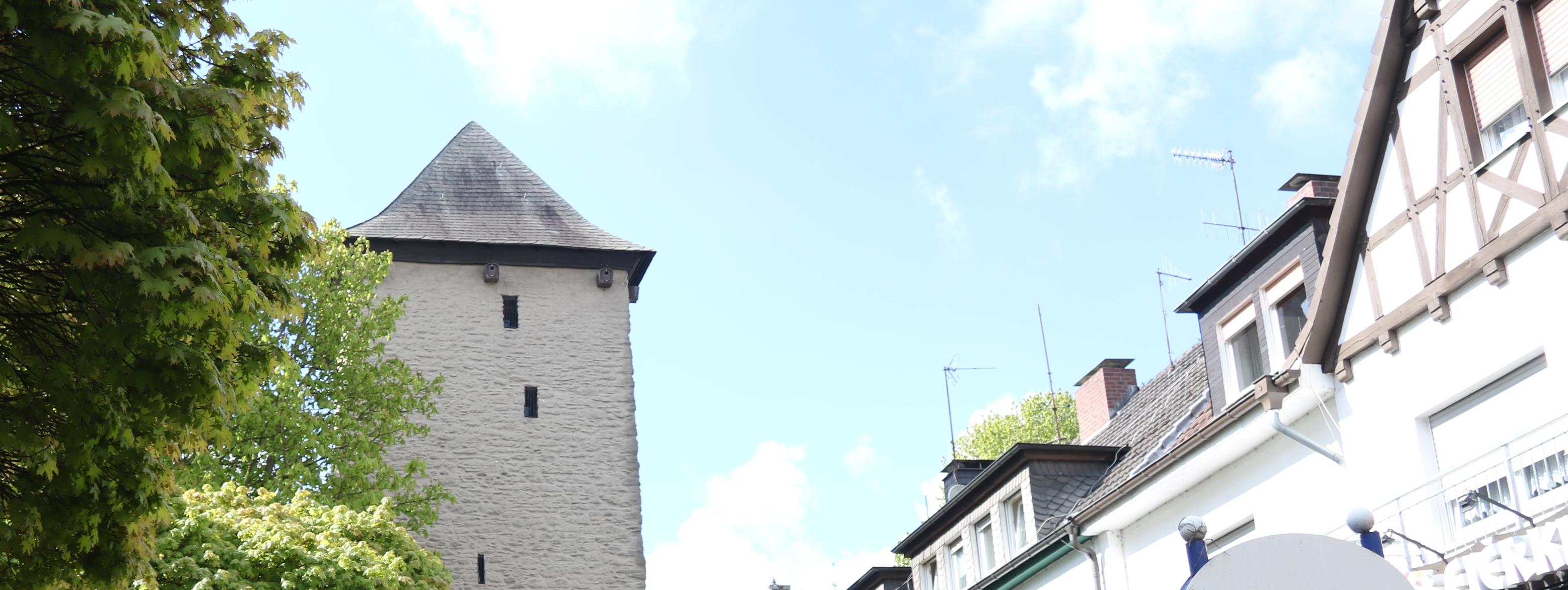 Der Poennigeturm, umringt von Bäumen auf der linken Seite und der Häuserfront der Turmstraße auf der rechten Seite.
