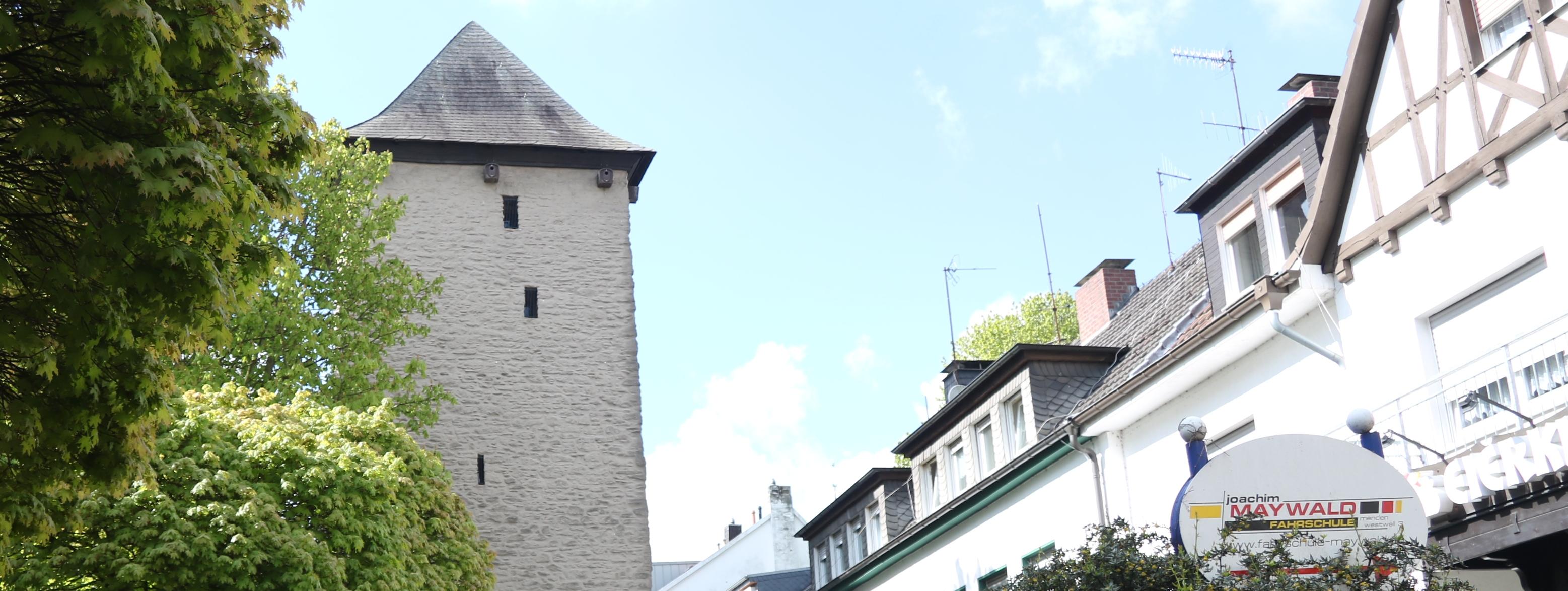 Der Poennigeturm, umringt von Bäumen auf der linken Seite und der Häuserfront der Turmstraße auf der rechten Seite.