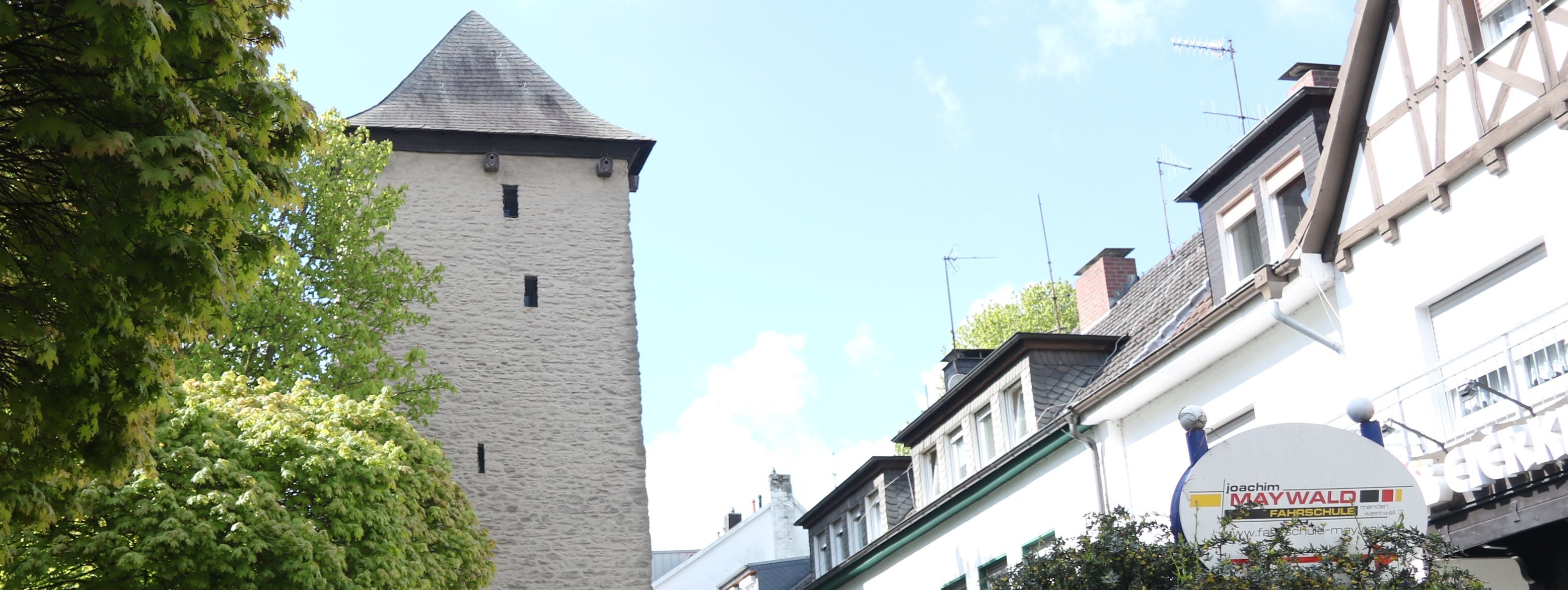 Der Poennigeturm, umringt von Bäumen auf der linken Seite und der Häuserfront der Turmstraße auf der rechten Seite.