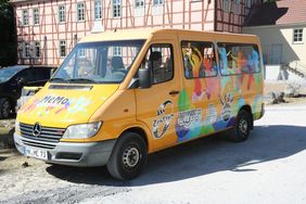 Das MEMO ist ein großer gelber Mercedes Sprinter. Auf dem Bus sind die Logos der Stadtteiltreffs und bunte Silhouetten von tanzenden Menschen geklebt worden.