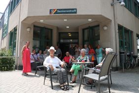 Vor dem Gebäude des Seniorentreffs sitzen Besucher in der Sonne.