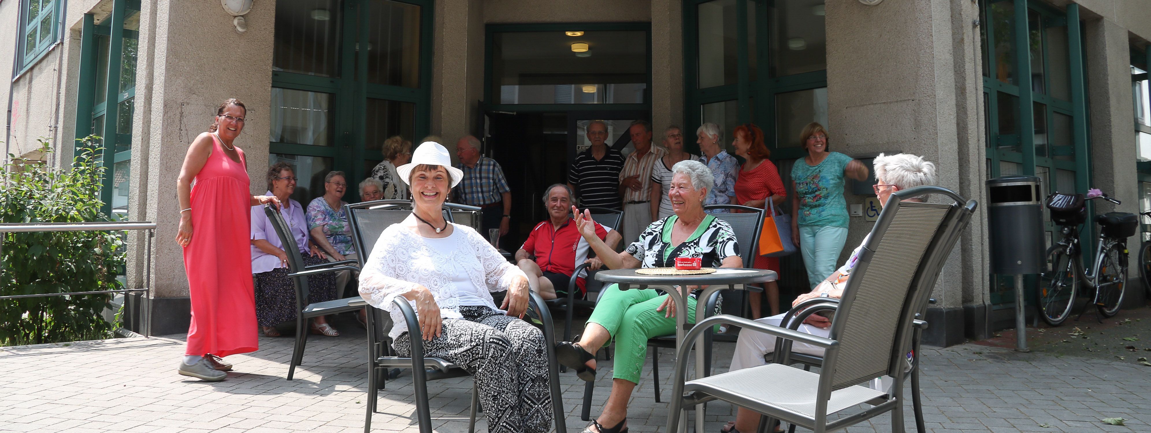 Vor dem Gebäude des Seniorentreffs sitzen Besucher in der Sonne.