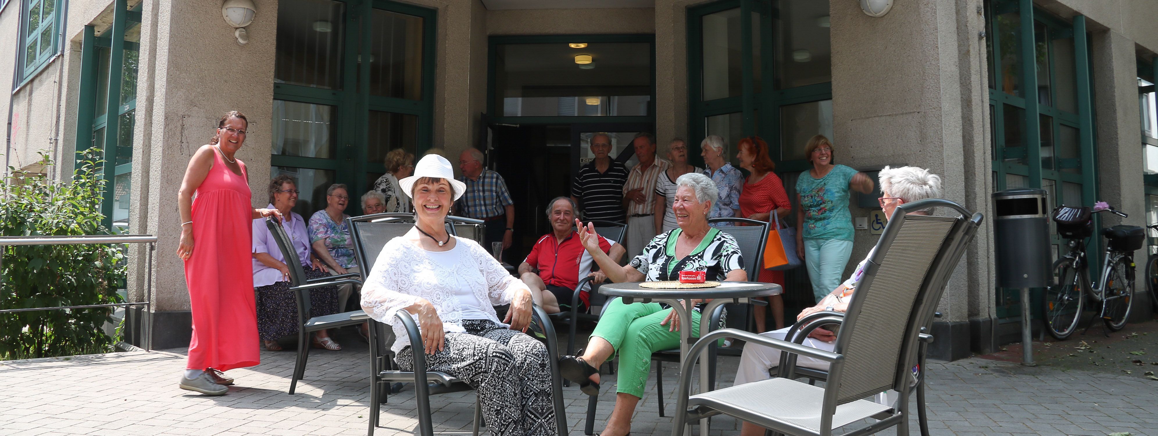 Vor dem Gebäude des Seniorentreffs sitzen Besucher in der Sonne.