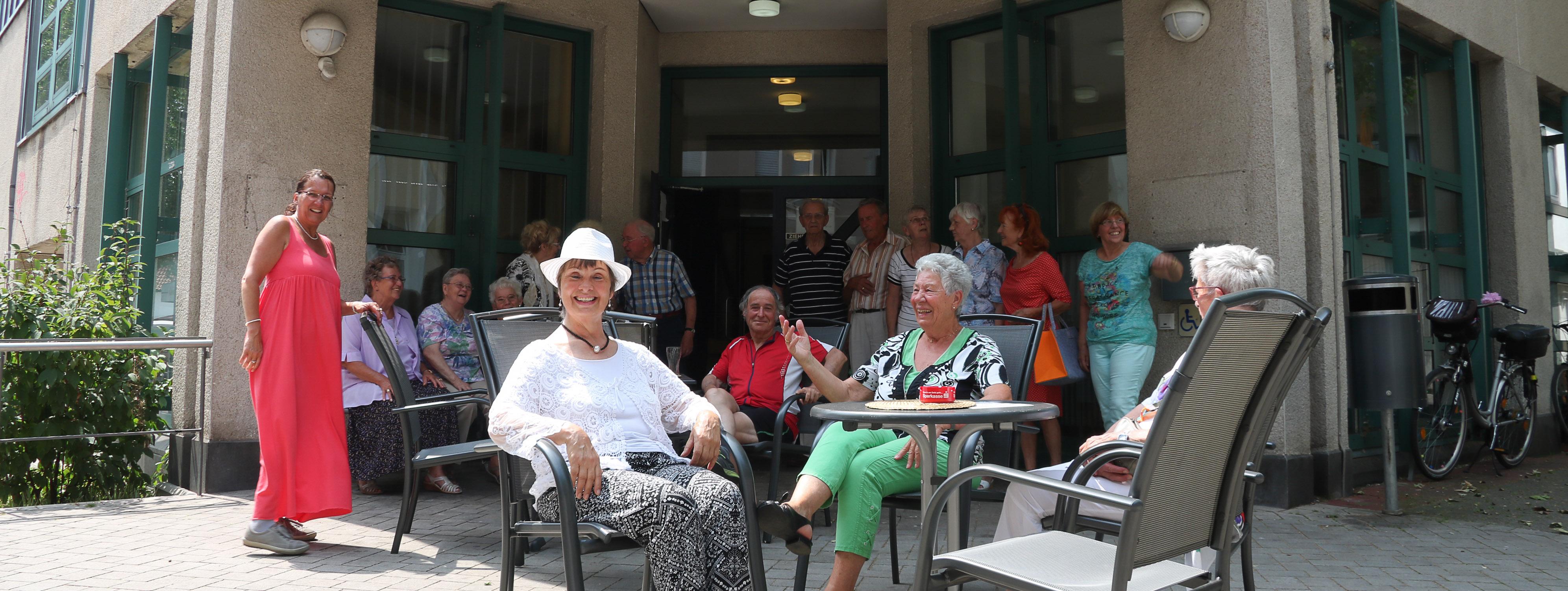 Vor dem Gebäude des Seniorentreffs sitzen Besucher in der Sonne.