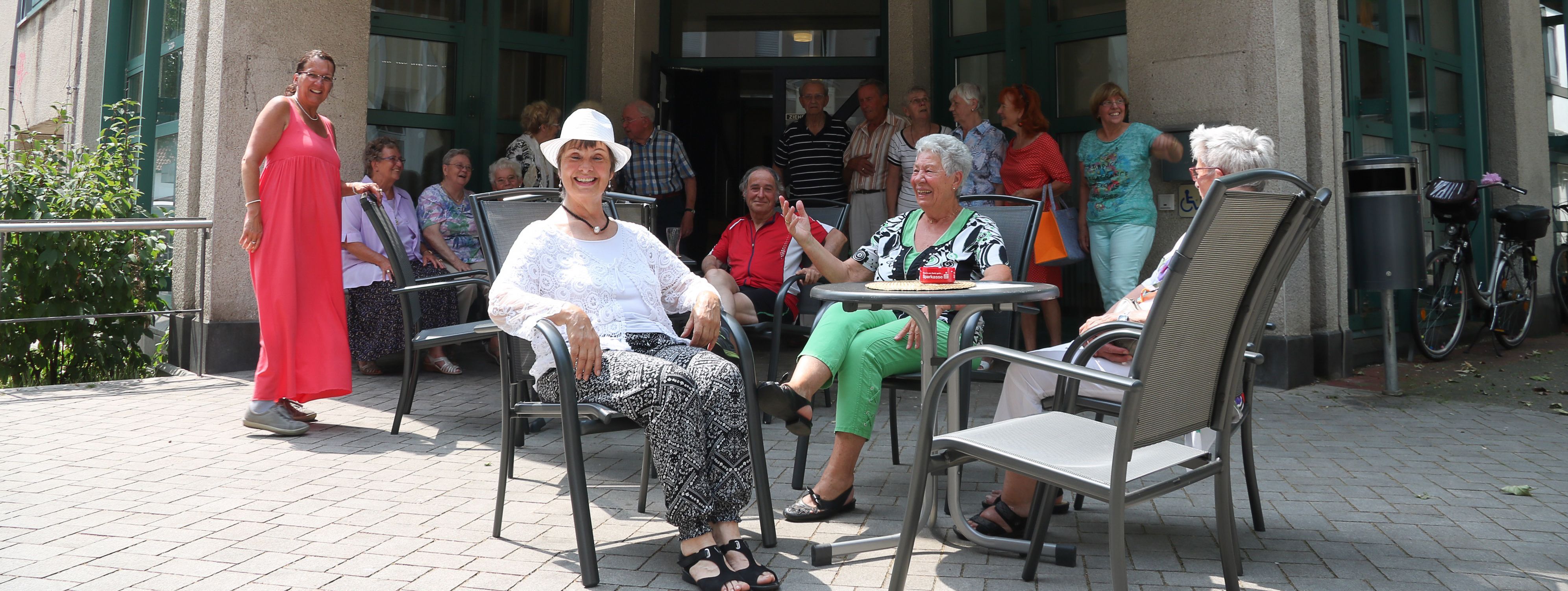 Vor dem Gebäude des Seniorentreffs sitzen Besucher in der Sonne.