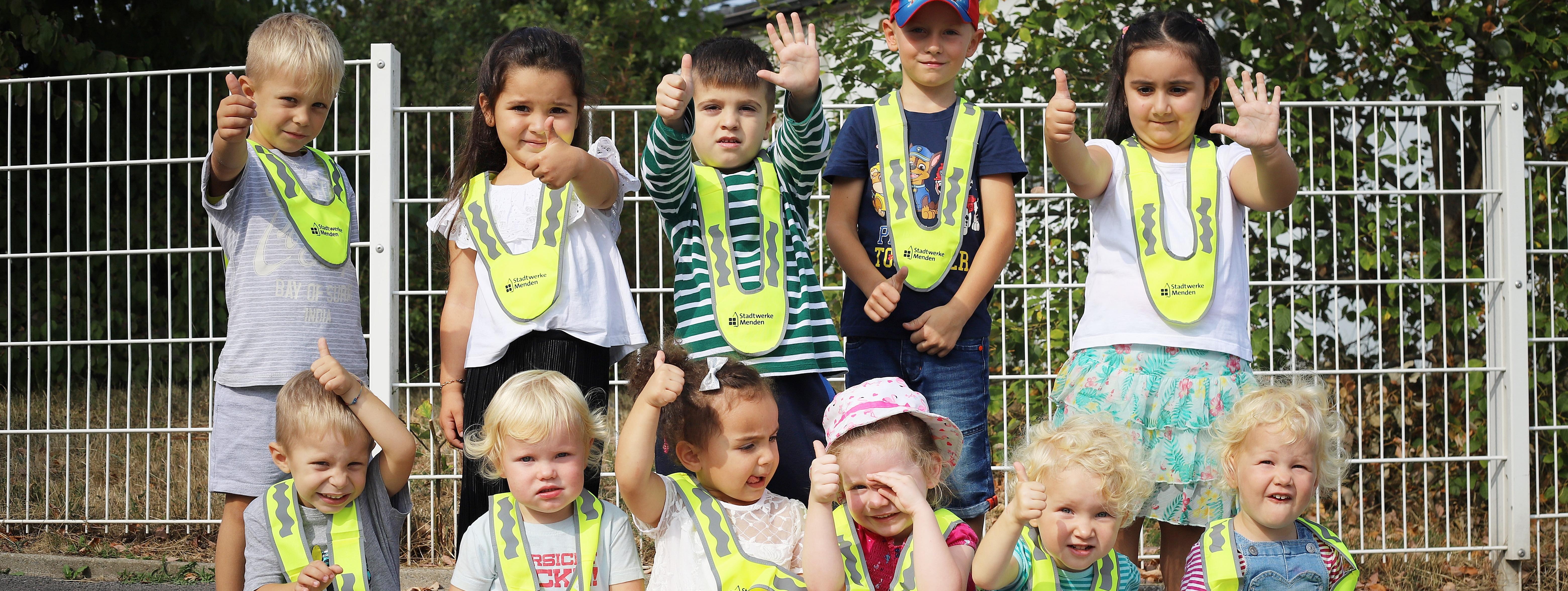 Die Kita-Kinder tragen ihre neuen Sicherheitskragen in leuchtendem Signal-Gelb. Alle Kinder strecken den Daumen nach oben.