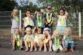 Die Kita-Kinder tragen ihre neuen Sicherheitskragen in leuchtendem Signal-Gelb. Alle Kinder strecken den Daumen nach oben.