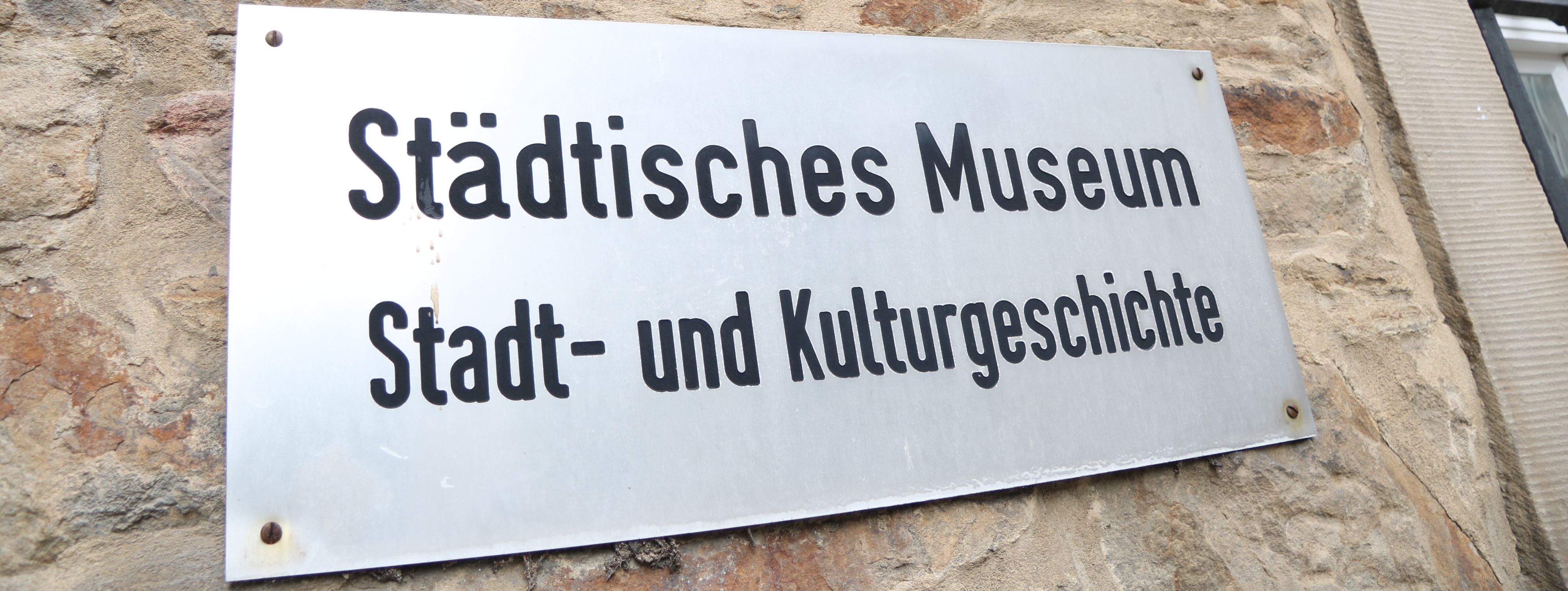 An der Außenwand des Stadtmuseums steht in großen Metallbuchstaben "Museum", darunter ist ein Metallschild mit der Aufschrift "Städtisches Museum für Stadt- und Kulturgeschichte