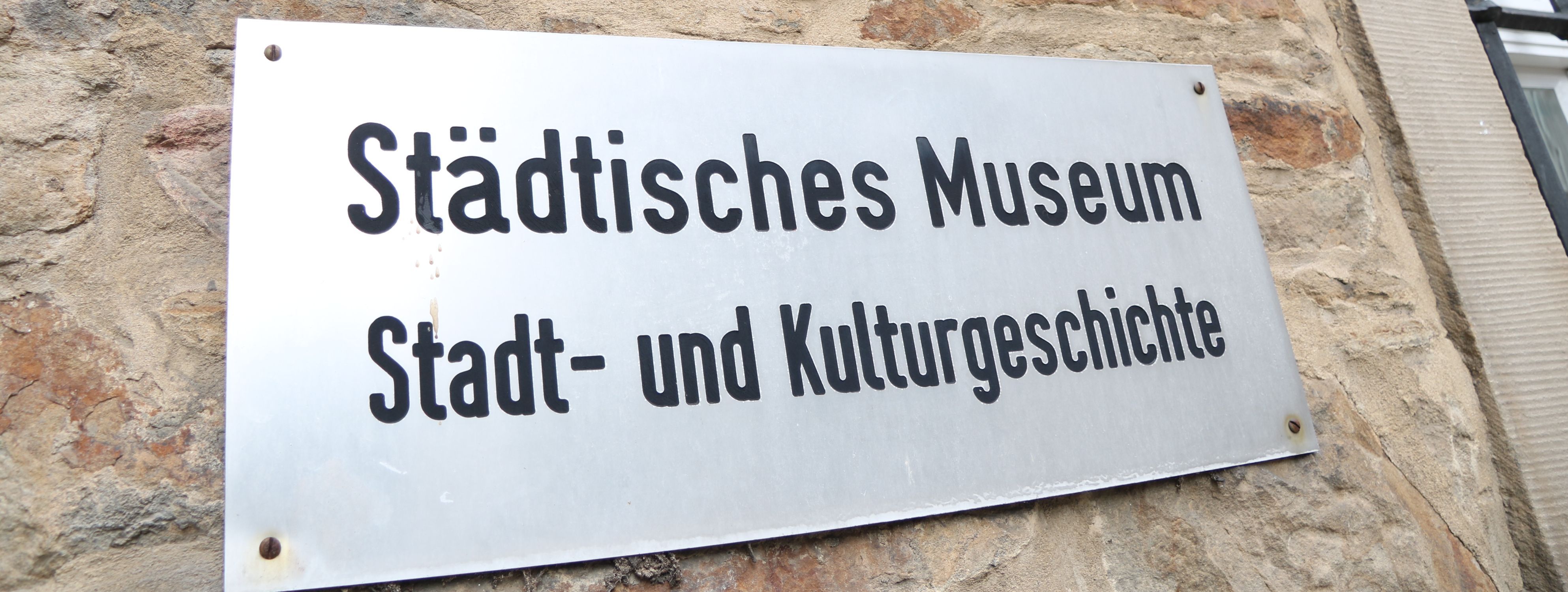 An der Außenwand des Stadtmuseums steht in großen Metallbuchstaben "Museum", darunter ist ein Metallschild mit der Aufschrift "Städtisches Museum für Stadt- und Kulturgeschichte