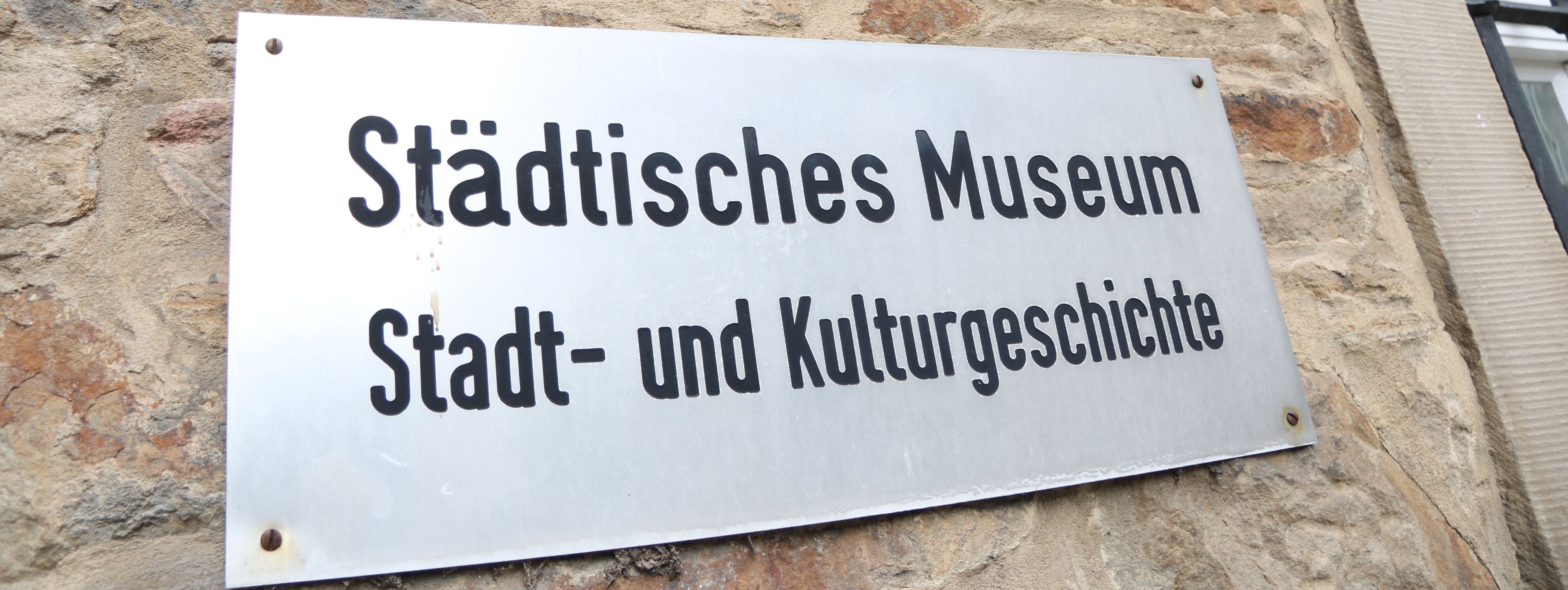 An der Außenwand des Stadtmuseums steht in großen Metallbuchstaben "Museum", darunter ist ein Metallschild mit der Aufschrift "Städtisches Museum für Stadt- und Kulturgeschichte