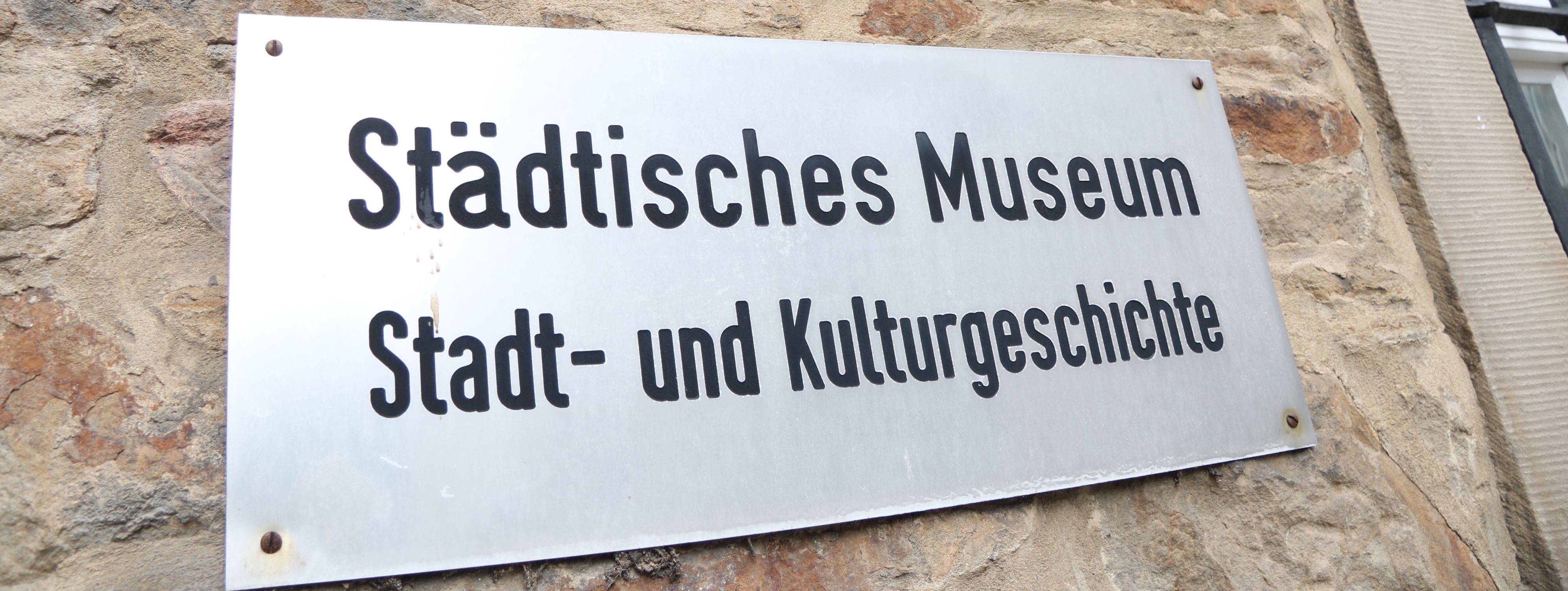 An der Außenwand des Stadtmuseums steht in großen Metallbuchstaben "Museum", darunter ist ein Metallschild mit der Aufschrift "Städtisches Museum für Stadt- und Kulturgeschichte