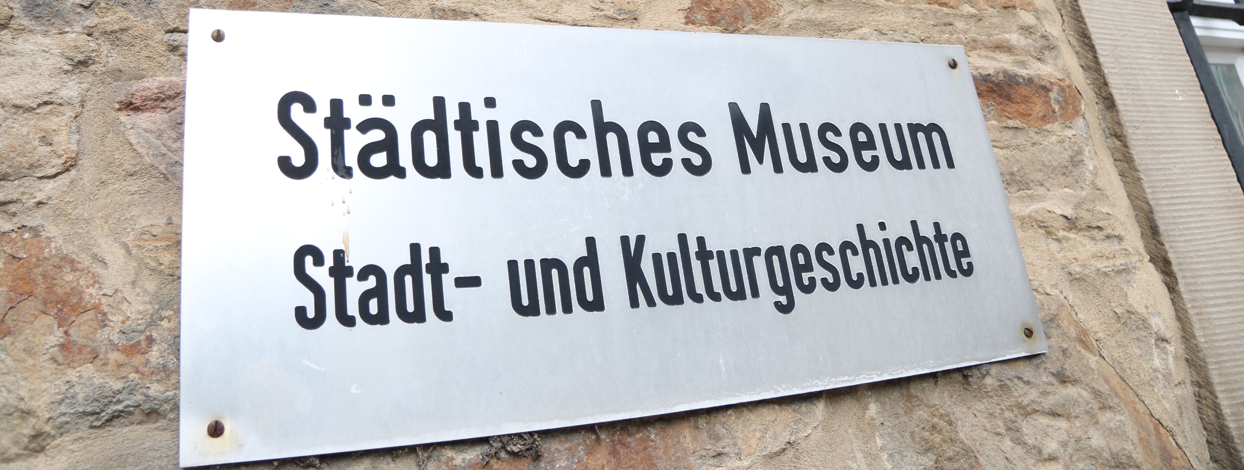 An der Außenwand des Stadtmuseums steht in großen Metallbuchstaben "Museum", darunter ist ein Metallschild mit der Aufschrift "Städtisches Museum für Stadt- und Kulturgeschichte