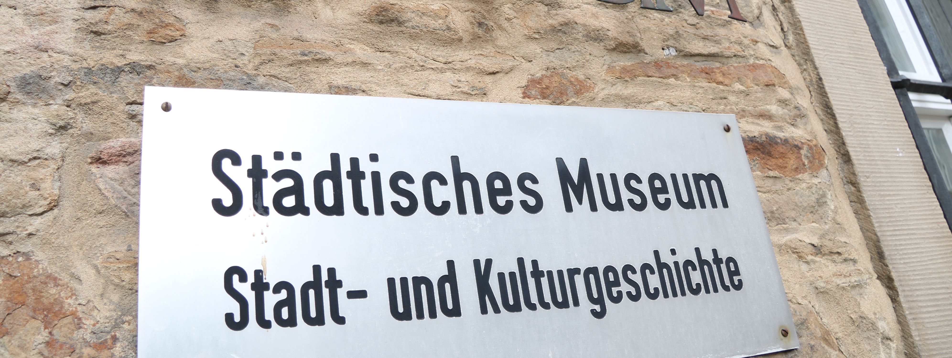 An der Außenwand des Stadtmuseums steht in großen Metallbuchstaben "Museum", darunter ist ein Metallschild mit der Aufschrift "Städtisches Museum für Stadt- und Kulturgeschichte