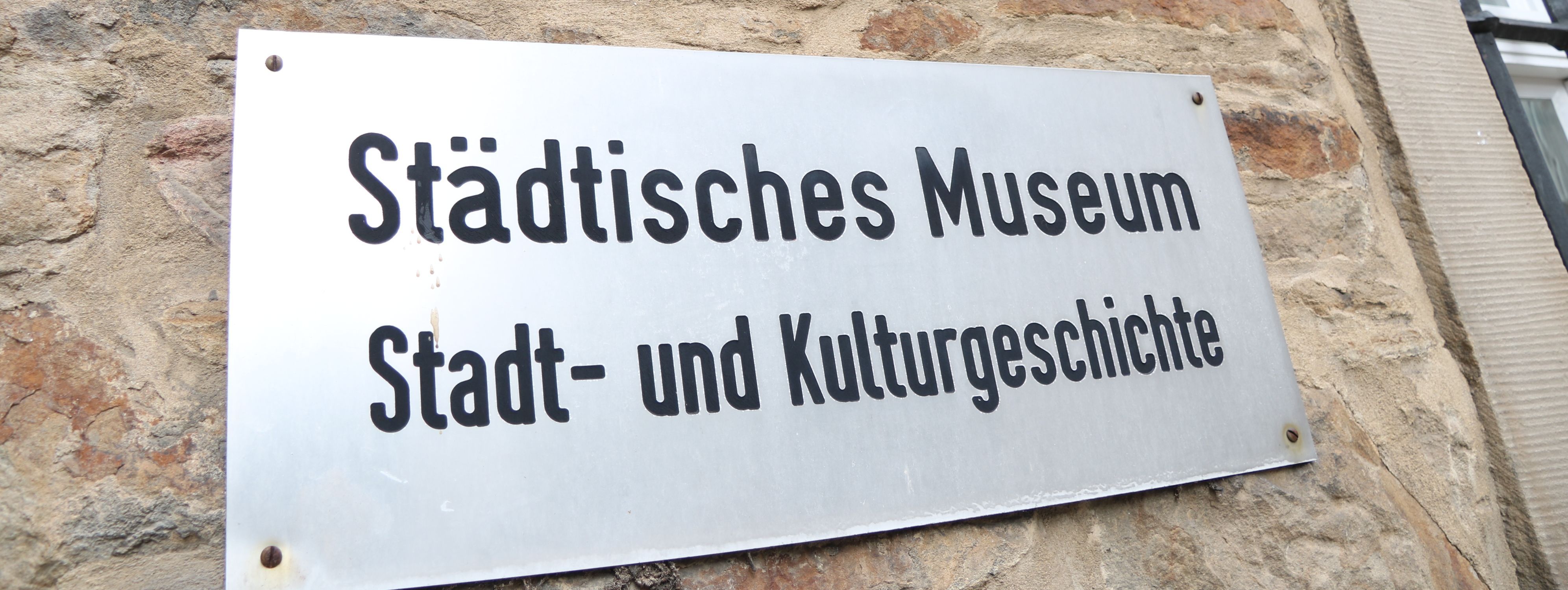 An der Außenwand des Stadtmuseums steht in großen Metallbuchstaben "Museum", darunter ist ein Metallschild mit der Aufschrift "Städtisches Museum für Stadt- und Kulturgeschichte