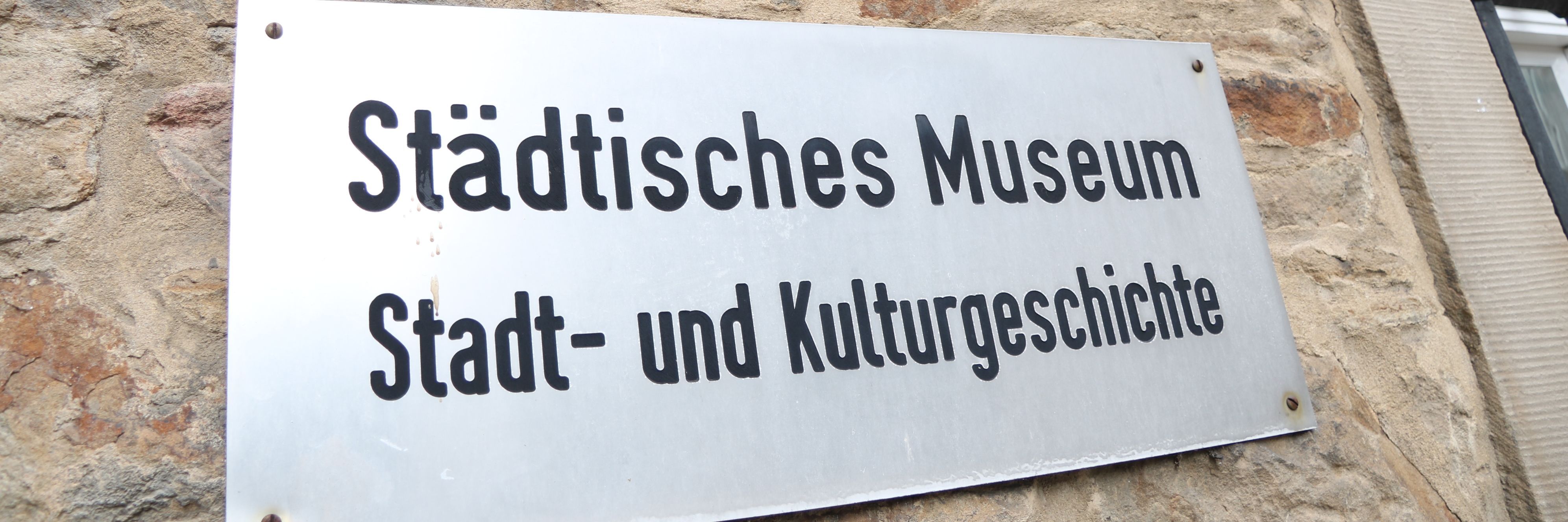 An der Außenwand des Stadtmuseums steht in großen Metallbuchstaben "Museum", darunter ist ein Metallschild mit der Aufschrift "Städtisches Museum für Stadt- und Kulturgeschichte