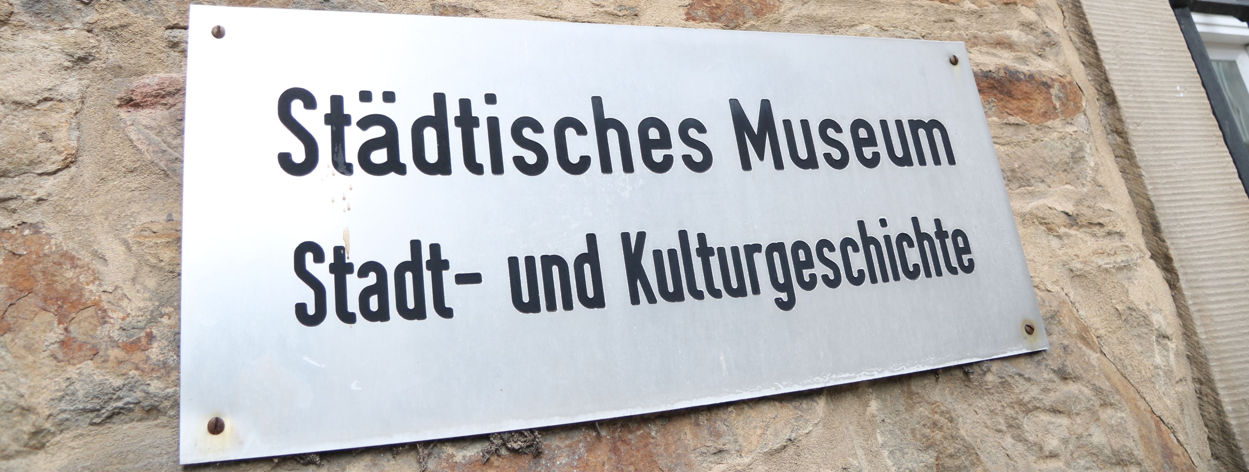 An der Außenwand des Stadtmuseums steht in großen Metallbuchstaben "Museum", darunter ist ein Metallschild mit der Aufschrift "Städtisches Museum für Stadt- und Kulturgeschichte