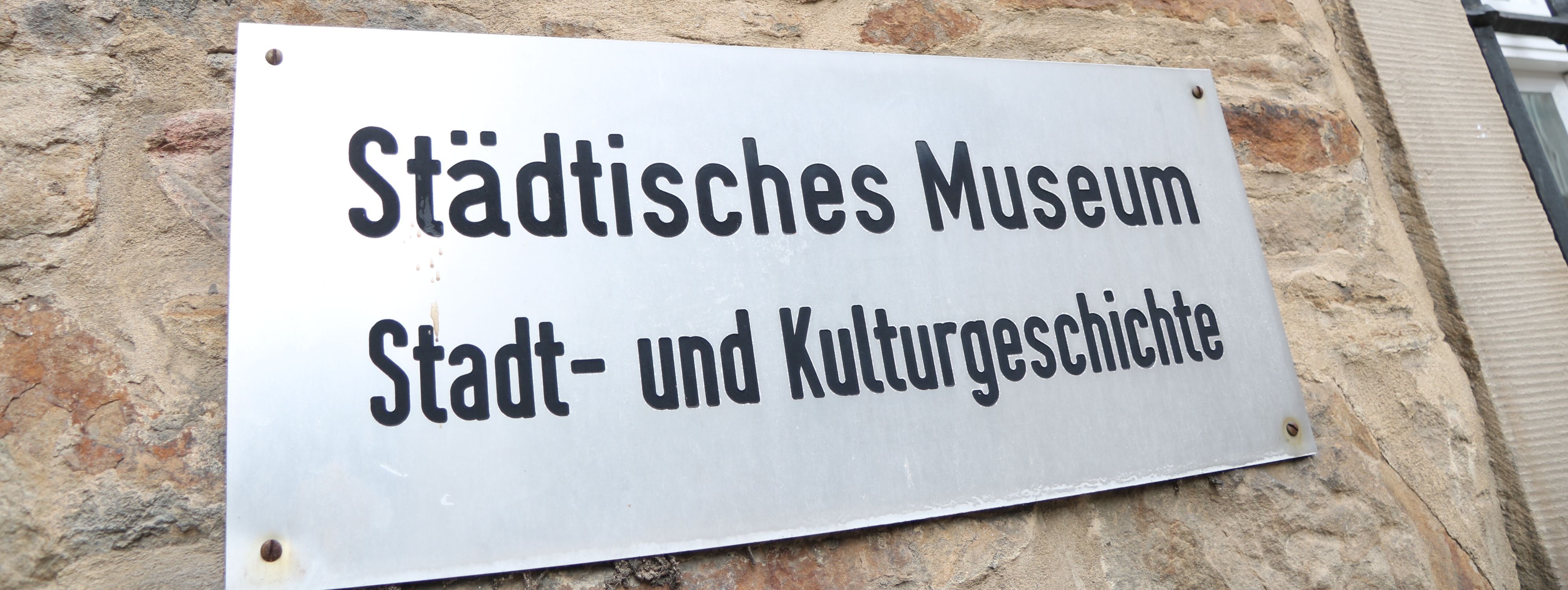 An der Außenwand des Stadtmuseums steht in großen Metallbuchstaben "Museum", darunter ist ein Metallschild mit der Aufschrift "Städtisches Museum für Stadt- und Kulturgeschichte