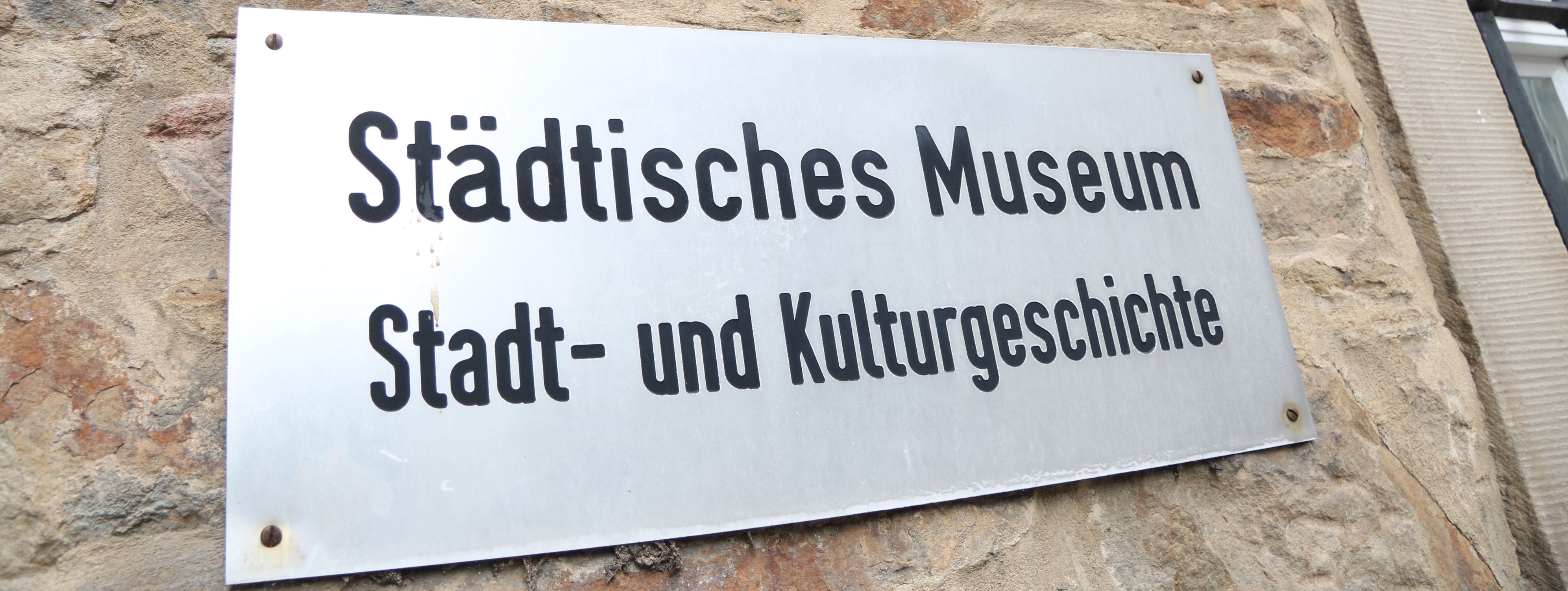 An der Außenwand des Stadtmuseums steht in großen Metallbuchstaben "Museum", darunter ist ein Metallschild mit der Aufschrift "Städtisches Museum für Stadt- und Kulturgeschichte