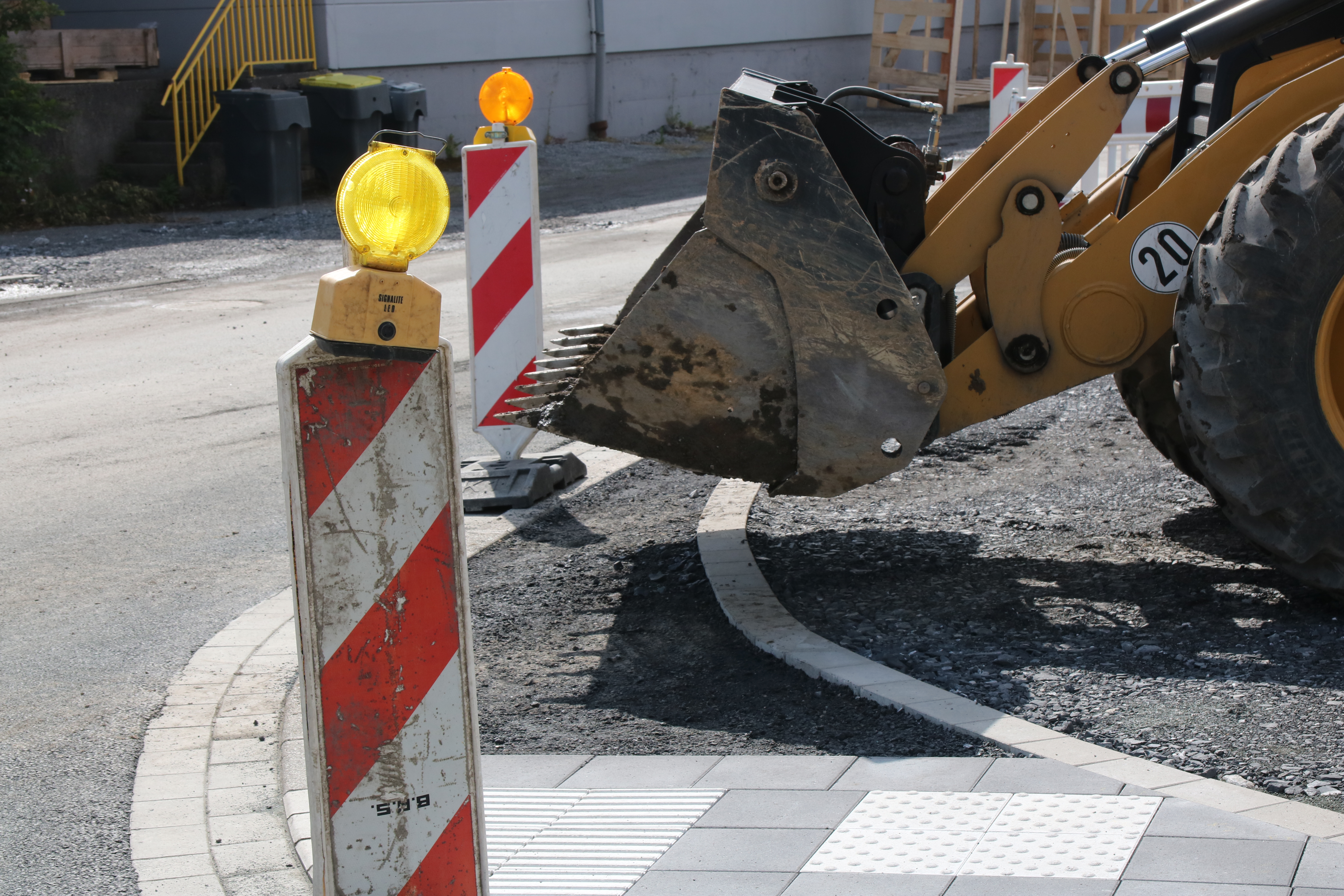 Im Vordergrund steht eine rot-weiße Bake mit gelber Warnleuchte darauf, im Hintergrund sieht man die Schaufel eines Radladers.