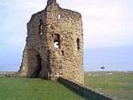 Zu sehen ist Castle Flintshire vor blauem Himmel umgeben von grüner Wiese. 